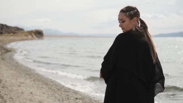 Menina oriental caminha ao longo das margens de um rio, vestido nacional preto — Vídeo de Stock