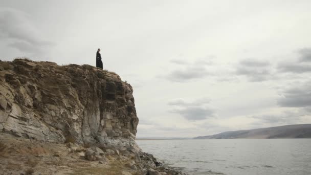 Muslimische Frau steht am Rande einer Klippe an der Spitze eines Berges, großer See — Stockvideo