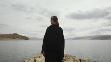 Dağın tepesindeki uçurumun kenarındaki kız gezgin. Büyük bir göl..