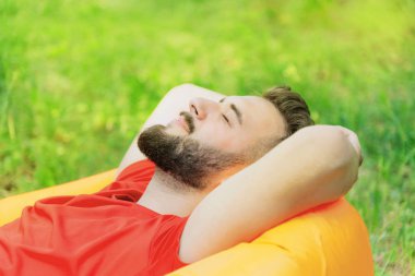 Genç adam parktaki şişme yatakta yatıyor, elleri başının arkasında.