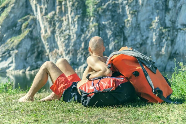 Człowiek Siedzi Trawie Czerwonym Plecakiem Patrzy Góry Koncepcja Podróży Turystyki — Zdjęcie stockowe