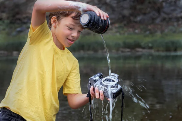 a boy in a yellow T-shirt pours water on a digital SLR camera. waterproof device concept