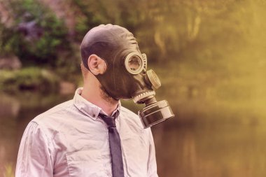 Beyaz gömlekli, gaz maskeli bir adam doğanın arka planında, enfeksiyon konsepti, kıyamet ve çevre kirliliği