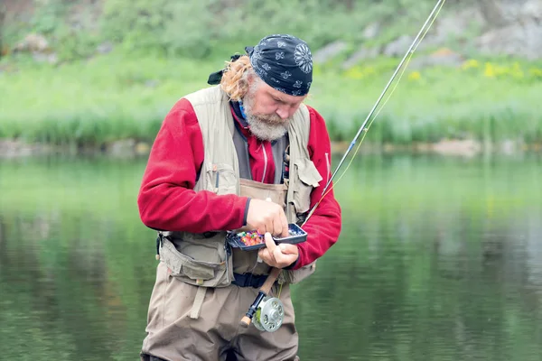 ひげとボダナを持つ男は自然を背景に釣竿を手にした漁具で箱から餌を選び — ストック写真