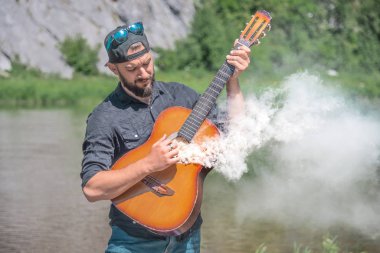 Doğada sigara içen akustik gitar çalan bir adam.