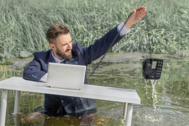 Bataklıkta takım elbiseli bir adam ıslak bir sabit telefonu suyun üzerinde tutuyor.
