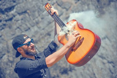 Şapkalı ve güneş gözlüklü bir adam sigara içen gitarla oynuyor.