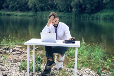 Takım elbiseli bir adam nehrin kenarındaki beyaz bir masada oturuyor. ofis işi kavramı