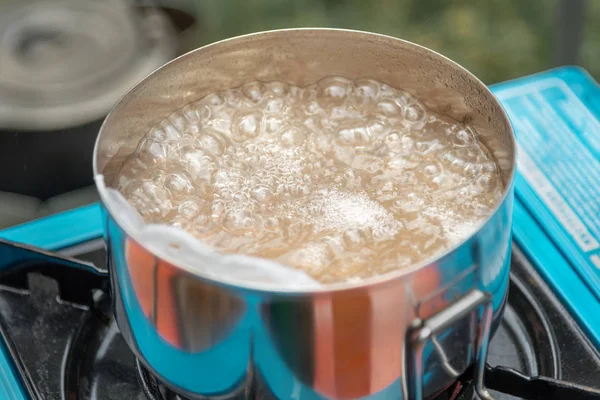 a steel pan with boiling water stands on a gas stove. cooking while camping