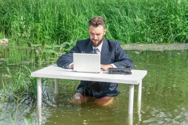 Ceketli ve kravatlı bir adam bataklıktaki beyaz bir masada pantolonsuz oturur ve dizüstü bilgisayara bakar. Ofis işi ve rutin faaliyetler kavramı