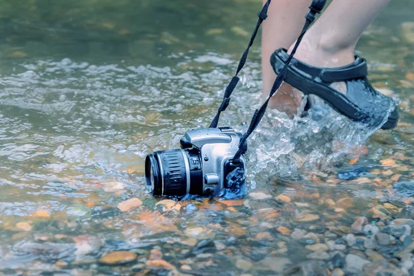 男は川の底の岩の上に水に浸かった一眼レフカメラをドラッグします 防水性と信頼性の高い装置の概念 — ストック写真