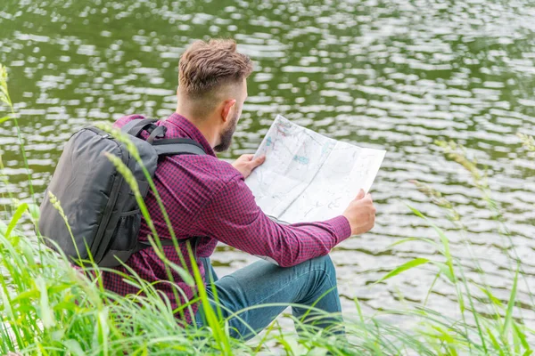 Mężczyzna Burgundowej Koszuli Dżinsach Plecakiem Nad Rzeką Tle Natury Patrzy — Zdjęcie stockowe