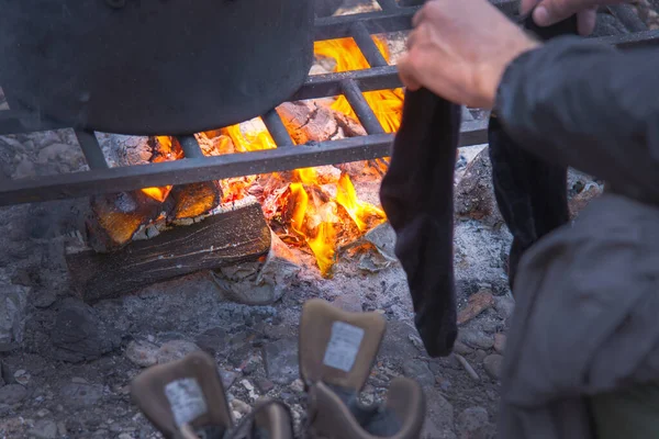 in the hands of socks by the fire. in the evening a tourist prepares food at the stake and dries clothes and boots