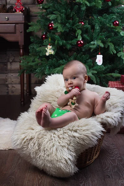 Baby boy with a wooden crocheted toy in the basket with white fur under the Christmas tree