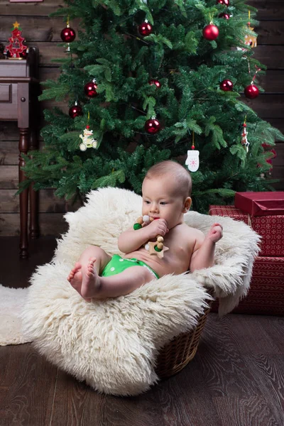 Baby boy with a wooden crocheted toy in the basket with white fur under the Christmas tree