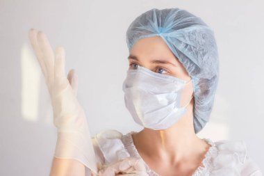 Tıbbi maske ve şapka takan kadın hemşire, tek kullanımlık eldiven takıyor. Koronavirüs enfeksiyonundan korunma, sağlık konsepti