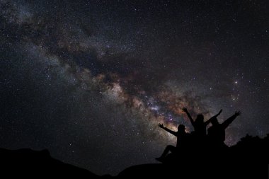 Yatay, Samanyolu, gece gökyüzünde yıldızlar ve mutlu insanlar silüeti dağlarda oturmak