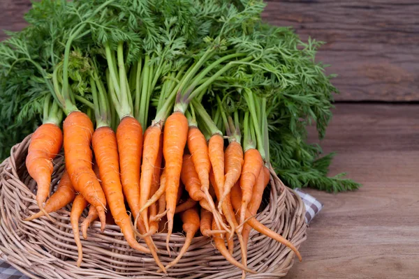 Bos van verse wortelen met groene bladeren op houten achtergrond — Stockfoto