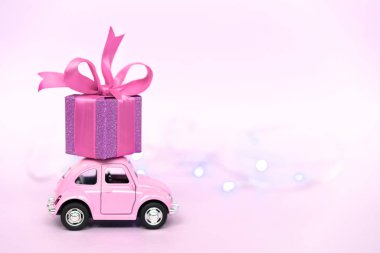 Pembe retro oyuncak araba, pembe arka planda Sevgililer Günü için hediye paketi teslim ediyor..