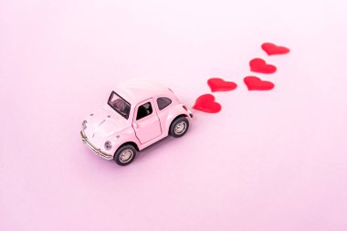  Pembe retro oyuncak kırmızı araba pembe arka planda kalp konfetisi. 