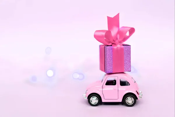 Rosa Retro-Spielzeugauto liefert Geschenkbox für Valentinstag auf rosa Hintergrund. — Stockfoto