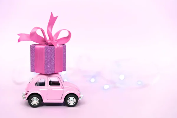 Рожевий ретро іграшковий автомобіль доставляє подарункові коробки для Валентинів день на рожевому фоні. — стокове фото