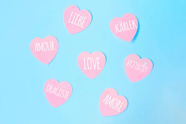 Algumas notas pegajosas cor-de-rosa em forma de coração com a palavra amor escrita em diferentes idiomas — Fotografia de Stock