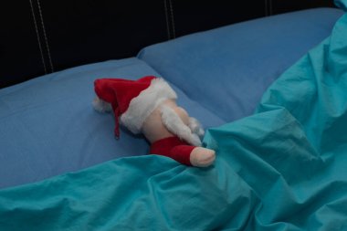 Noel Baba yorganla kaplı yatakta uyur. O yorgun ya da hasta ya da Noel günü için dinleniyor. Oyuncak bebek.