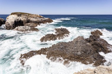 Deniz dalgaları beyaz köpükle kıyı kayalarının üzerinden geçiyor..