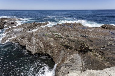 Kıyıda taş var. Okyanus dalgaları kıyıda sörf yapıyor..