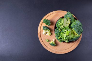 Ahşap mutfak tabağı ve siyah arka planda yeşil brokoli. Kopyalama alanı olan düz