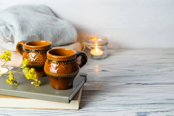 Hygge composition with two rustic cups of tea, books, candles and knitted plaid on white wooden background — Stock Photo, Image