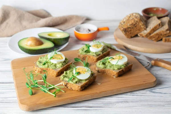 Healthy toasts with whole grain bread, avocado and boiled egg on wooden board