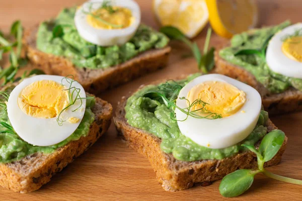 Healthy toasts with whole grain bread, avocado and boiled egg on wooden board.