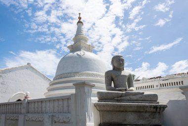 Önünde bir Buda heykeli olan mütevazı bir Budist beyaz tapınağı ve güzel bulutlu mavi bir gökyüzüne karşı. Galle, Sri Lanka