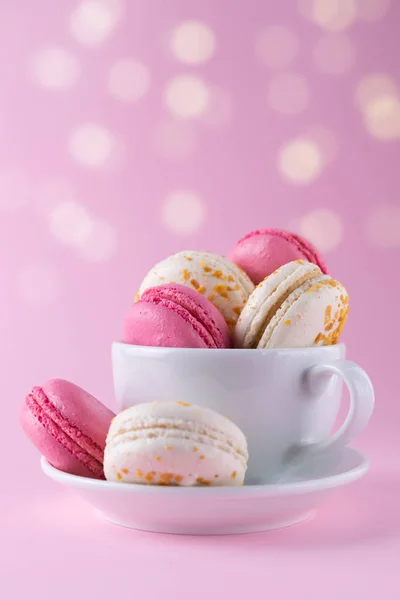 French pink and white delicious macarons in a coffee cup on pink pastel background