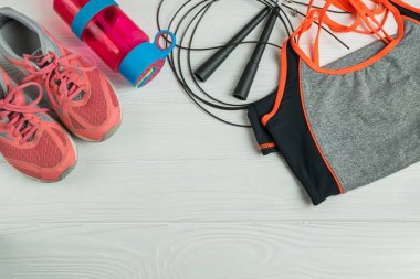 Kadın spor formalı sporcular, ip atlama, su için pembe parlak şişe ve beyaz tahta arka planda spor ayakkabıları. Düz yatıyordu. Metnin için kopyalama alanı