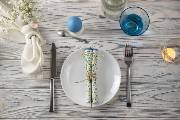 Świąteczny stół Wielkanocny na białym drewnianym stole z dekoracjami wielkanocnymi, świecą, serwetką i farbowanymi jajkami — Zdjęcie stockowe