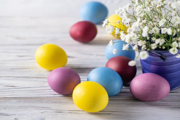 Feliz Pascua coloridos huevos teñidos con flores blancas de primavera en un cubo sobre fondo de madera blanca — Foto de Stock