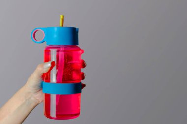 Kadın elinde spor yapmak için gri arka planda parlak pembe bir eko su şişesi tutuyor. Sağlıklı yaşam tarzı, yoga ve zindelik kavramı. Metnin için alanı kopyala