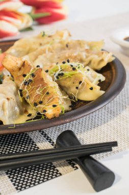 Japon Gyoza 'sı ya da hamur köftesi aperatifi geleneksel siyah tabakta ve yemek çubukları, soya sosu ve çiçeklerle mikro yeşil kaplı Japon ve Çin mutfağı..