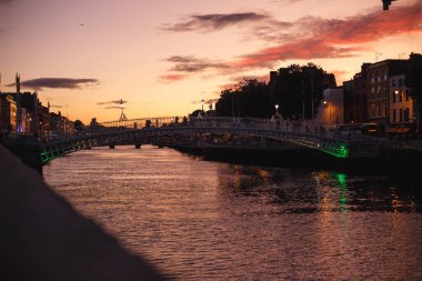 Dublin 'in renkli günbatımında Liffey nehri üzerinde bulutlar ve martılarla dolu şehir manzarası.