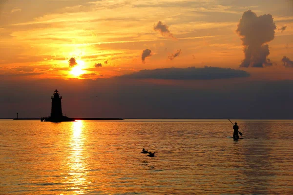 Silhouet van een licht huis en een man op een paddle board bij zonsondergang in Cape Henlopen State Park, Lewes, Delaware, Verenigde Staten — Stockfoto