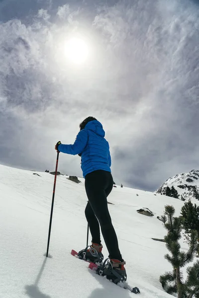 높은 산에서 눈 라켓을 든 채걷고 있는 젊은 여자 — 스톡 사진