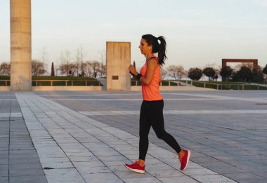 Gün batımında koşarken atlayan zinde genç bir kadın. Fitness ve sağlıklı yaşam tarzı