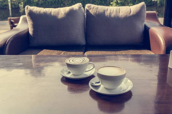 Filiżanek kawy na drewniany stół z przodu wygodną sofę. — Zdjęcie stockowe