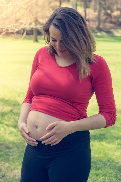 Pregnant woman wearing red shirt gently caressing her belly. — Stock Photo, Image