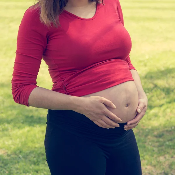 Gravid kvinna iklädd röd skjorta försiktigt smeka hennes mage. — Stockfoto