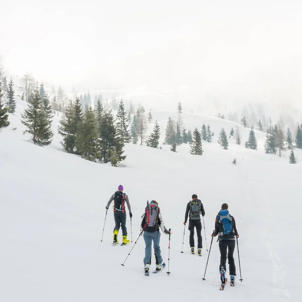 Group of back country skiers walking through a misty valley. — Stock Photo, Image