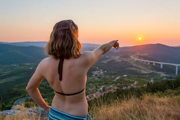 Attraktive Brünette zeigt auf die untergehende Sonne. — Stockfoto